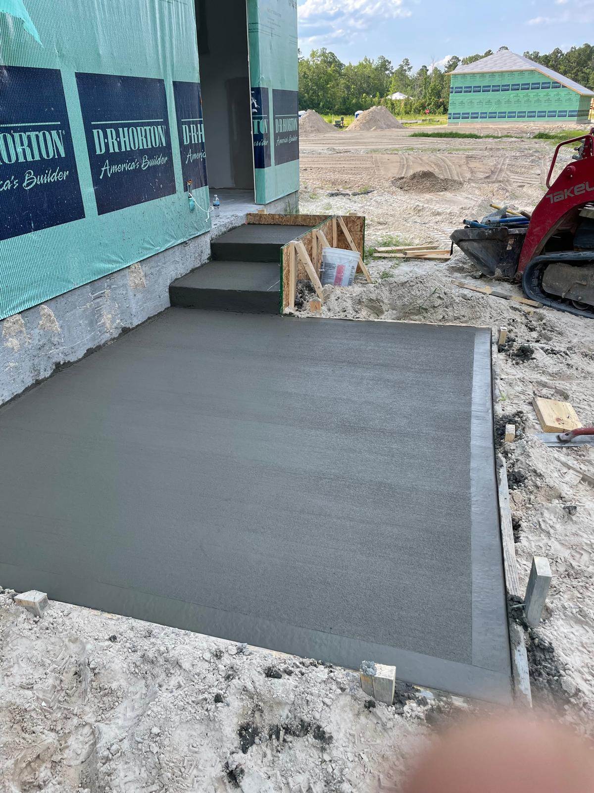 Freshly finished concrete patio and formed steps at the rear of a house under construction