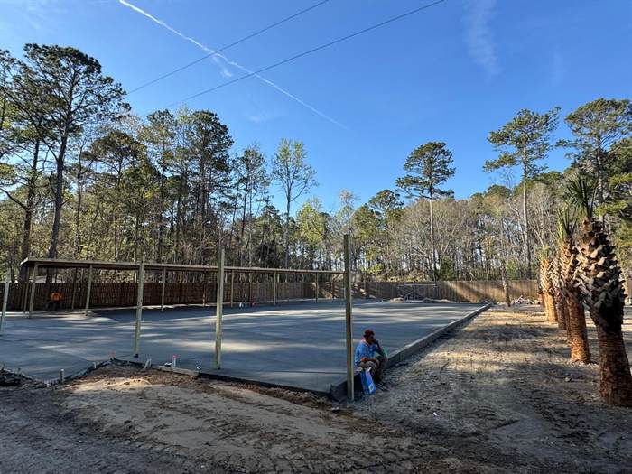 Completed large concrete pad beside a covered structure with palm trees in the background