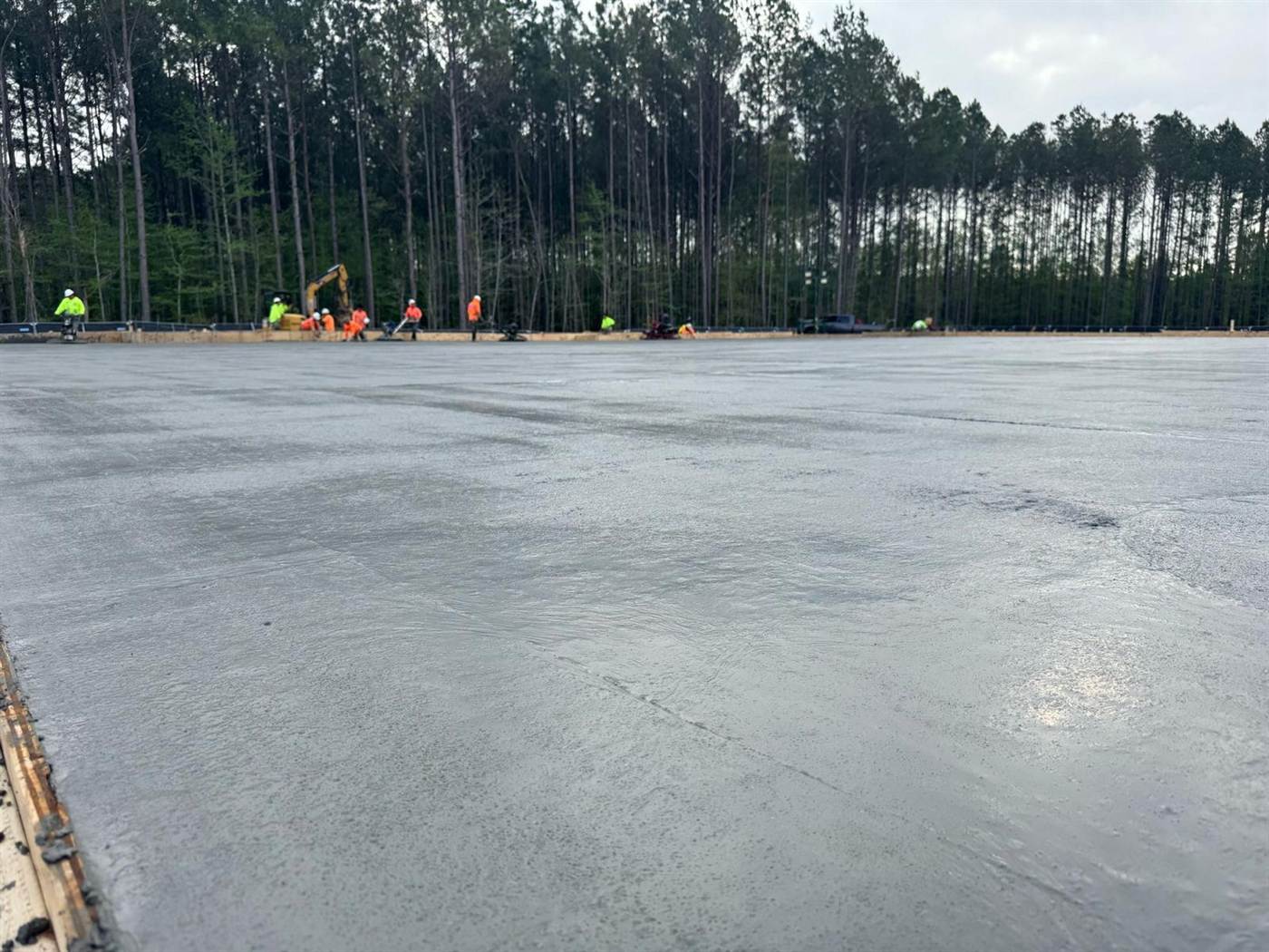 Large commercial concrete slab being finished by a crew in high-visibility vests along the formed edge
