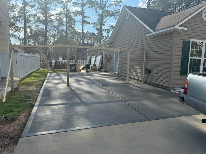 Finished concrete pad extending a driveway under a covered carport structure