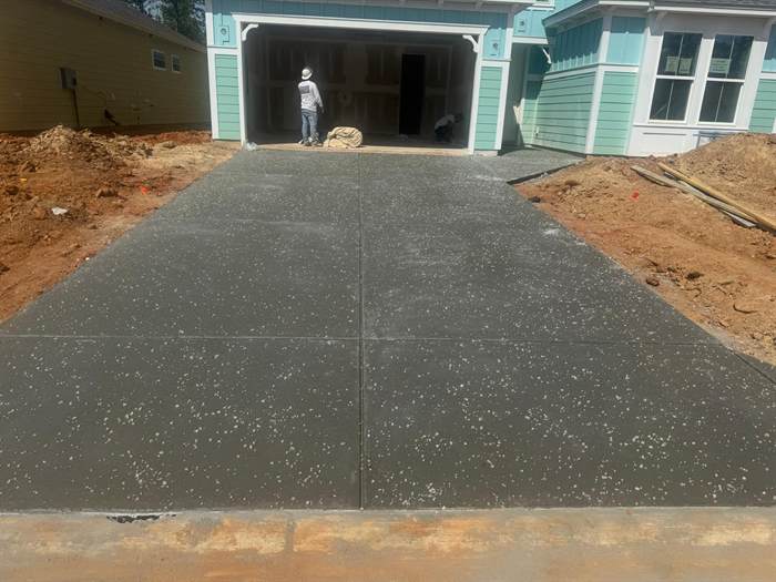 Freshly finished concrete driveway leading to the garage of a coastal style home with teal siding