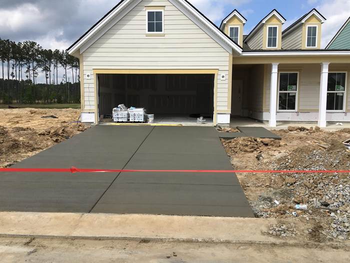 Newly poured concrete driveway and walkway in front of a home under construction, taped off to cure