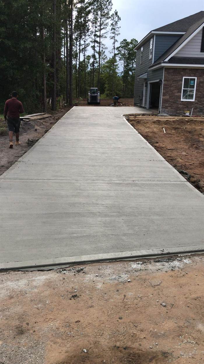 Long concrete driveway running from the road through a wooded lot to a new home garage