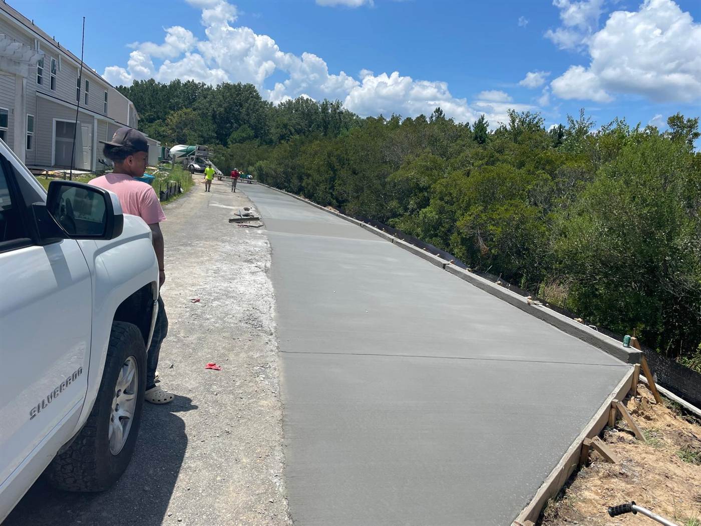 Long ribbon of freshly finished concrete driveway formed along a graded slope beside new townhomes
