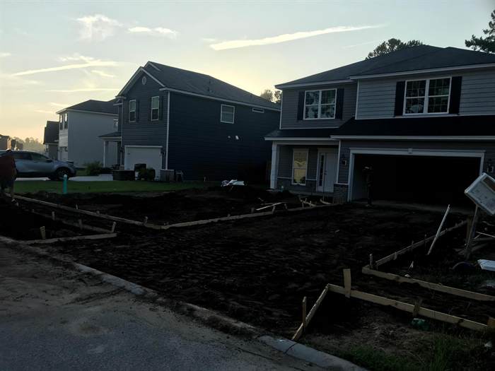 Driveway subgrade graded and formed with staked timber edges in front of a home at dusk