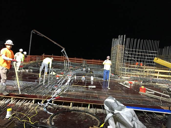Night pour of an elevated reinforced concrete deck with column cages and a boom pump