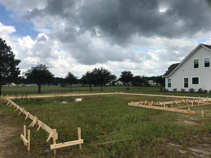 House footprint laid out with staked timber forms and batter boards on a cleared residential lot