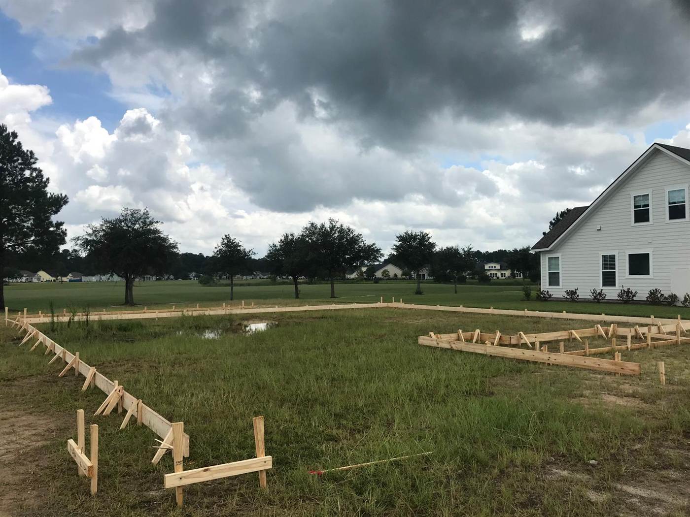 House footprint laid out with staked timber forms and batter boards on a cleared lot before excavation