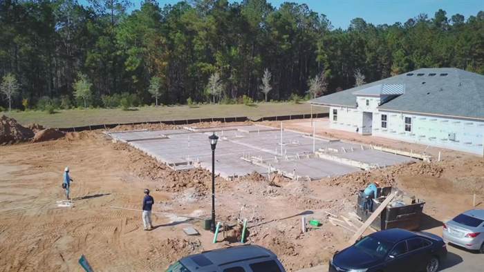 Aerial view of a formed and prepared foundation next to a house already framed and roofed