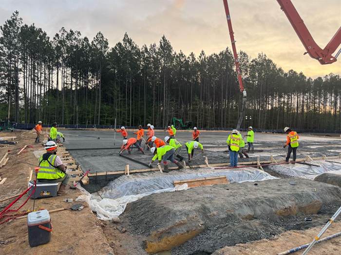 Full crew placing and screeding a large slab at dusk while a boom pump delivers concrete