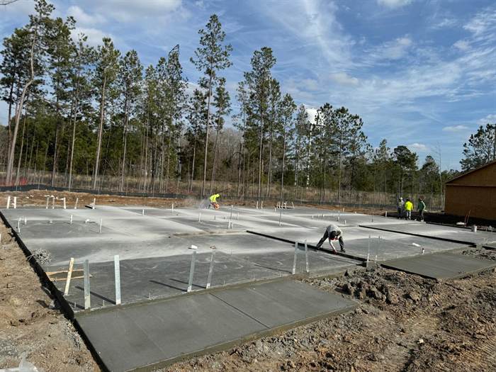 Several finished building slabs with anchor bolts set and a worker saw cutting control joints