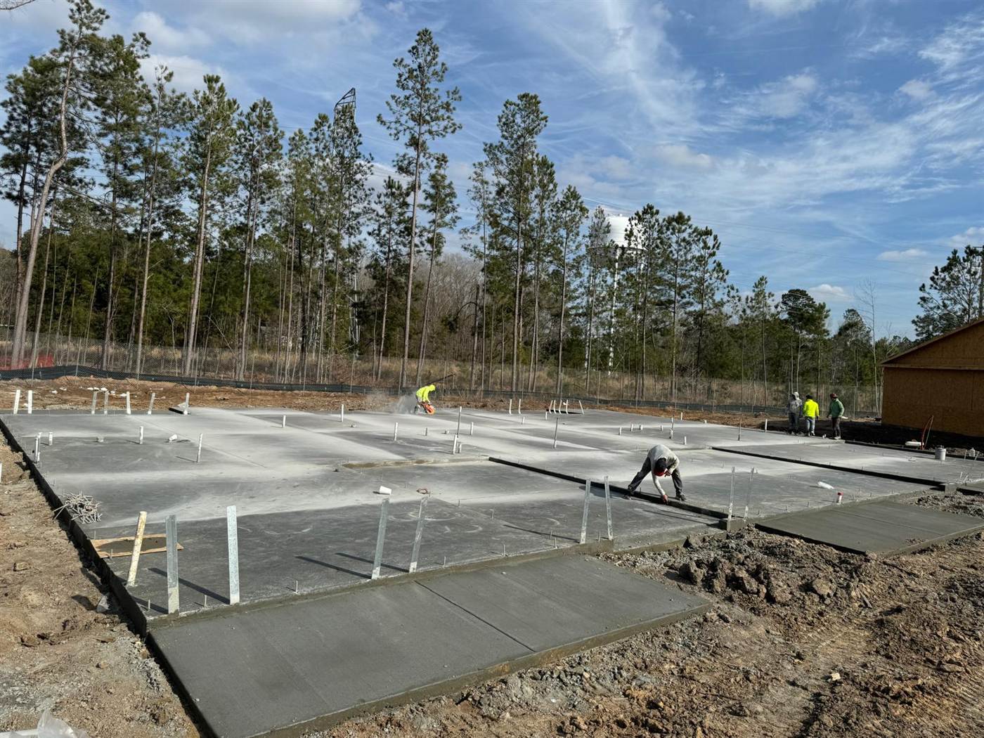 Multiple finished residential slabs on one site with anchor bolts set and control joints being saw cut