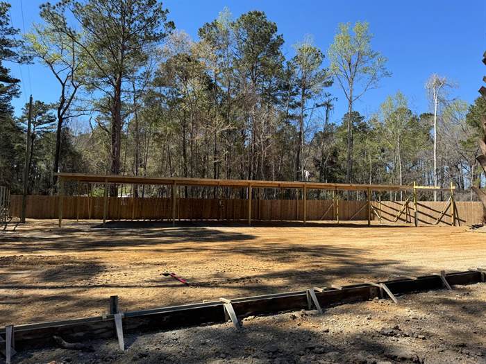 Perimeter forms staked out in a graded yard in front of a long open pole barn structure
