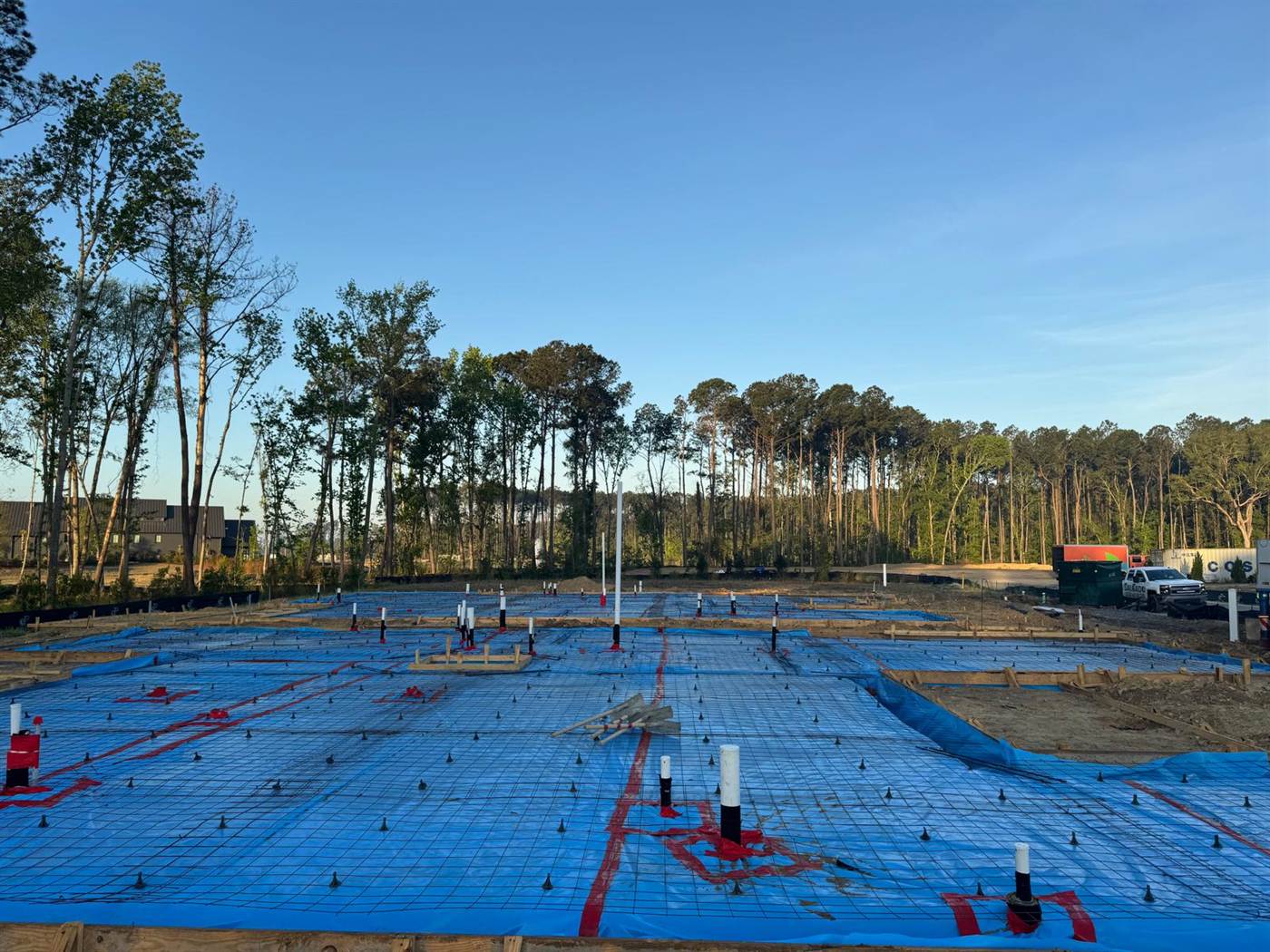 Foundation prepared for pouring with blue vapor barrier, reinforcing mesh on chairs, plumbing sleeves and marked layout lines