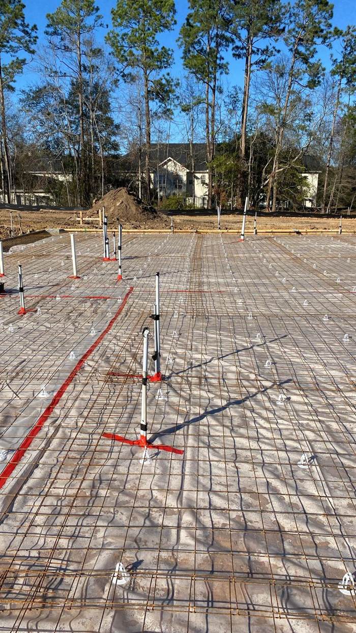 Reinforcing mesh on chairs over a vapor barrier with screed pins and a laser line across a foundation