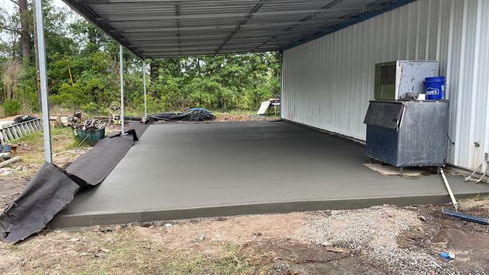 Freshly poured and floated concrete slab under a metal roofed lean-to beside a shop building
