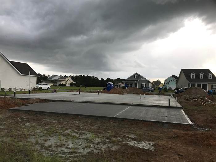 Completed residential slab and driveway pad under a dark storm sky with crew still on site