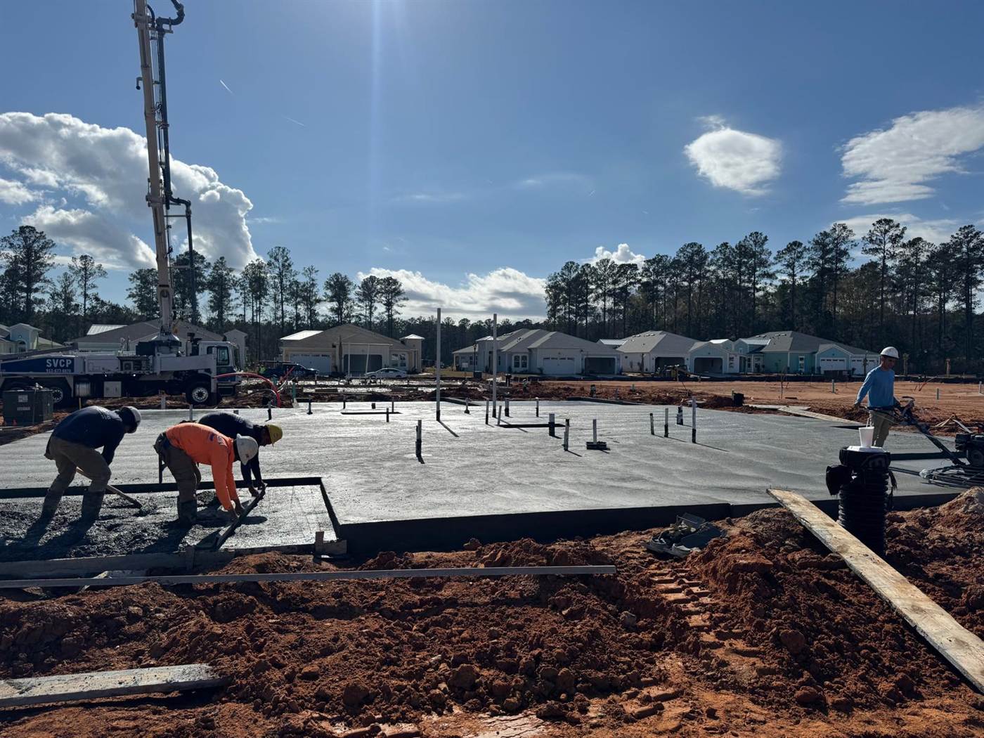 Crew screeding a residential slab as a concrete pump places the pour in a new home community