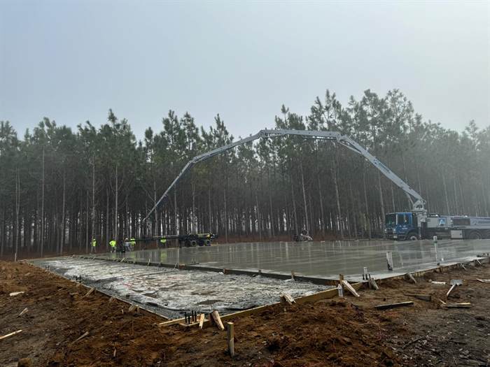 Concrete pump boom extended over a large freshly finished slab in a cleared wooded lot