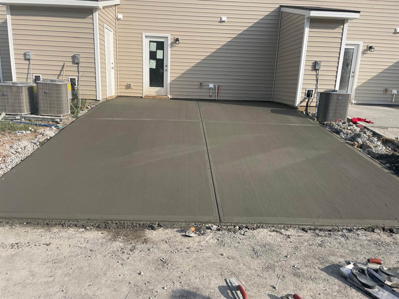 Finished concrete patio slabs and equipment pads running along the rear of a row of new townhomes